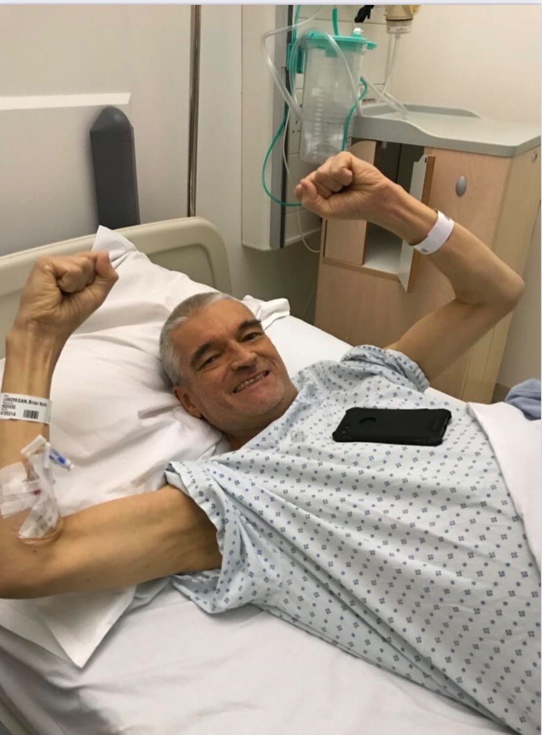 Brian celebrating in a hospital bed with both fists raised after his liver transplant